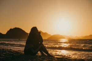 Kvinde alene på stranden og kigger på solnedgang og tænker over livet. Livskriser
